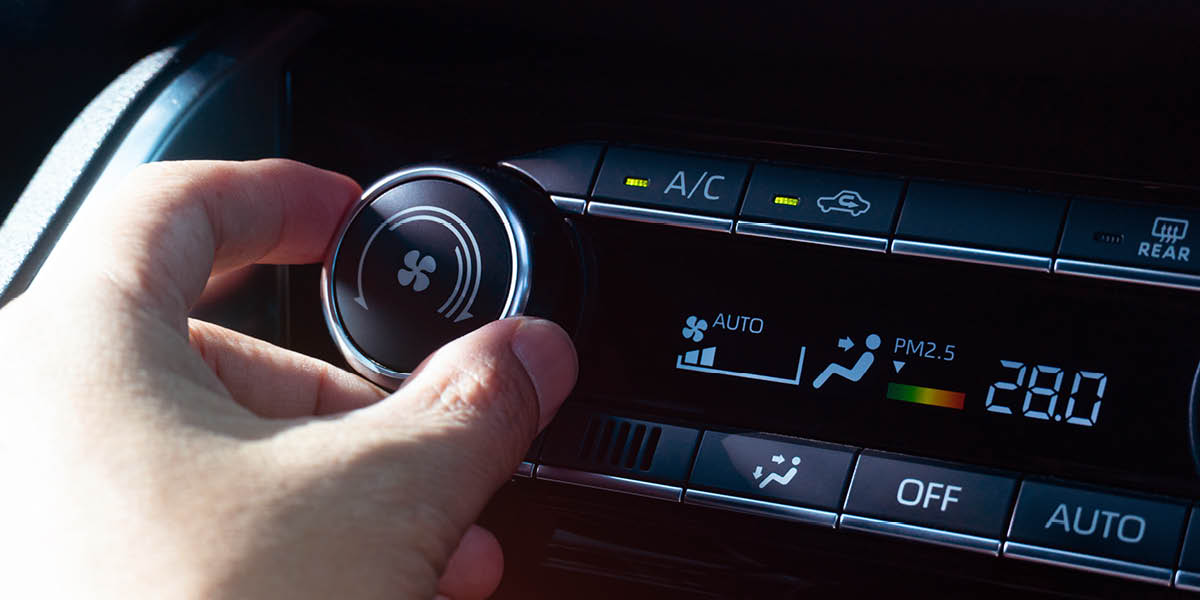 Eine Hand bedient einen Drehregler für die Klimaanlage im Auto, angezeigt wird die Temperatur und Luftzirkulation.