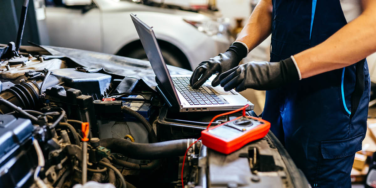 Ein Mechaniker arbeitet mit Laptop und Messgerät am offenen Motor eines Autos.